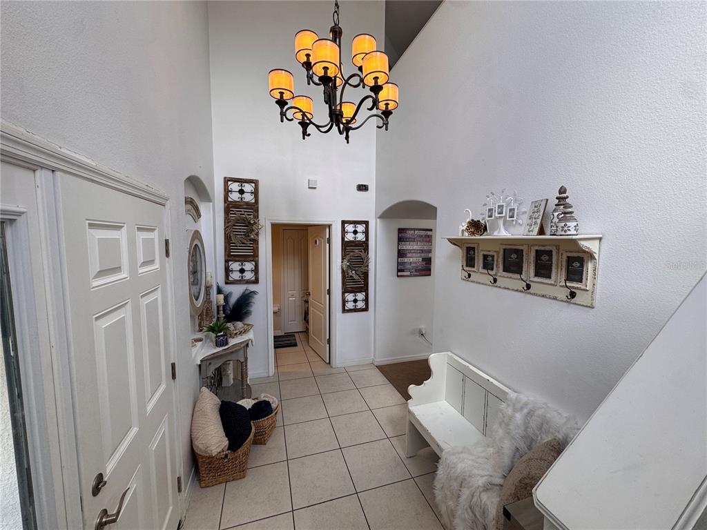 A bright entryway features a high ceiling, a chandelier, tile flooring, and a white bench — 2232 COLVILLE CHASE DRIVE, RUSKIN, FL