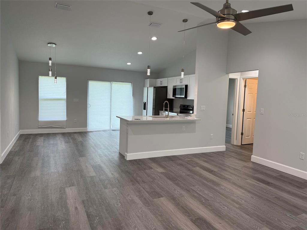 An open-concept kitchen and living area features gray wood-look flooring and white cabinetry — 15854 SW 38 PLACE, OCALA, FL