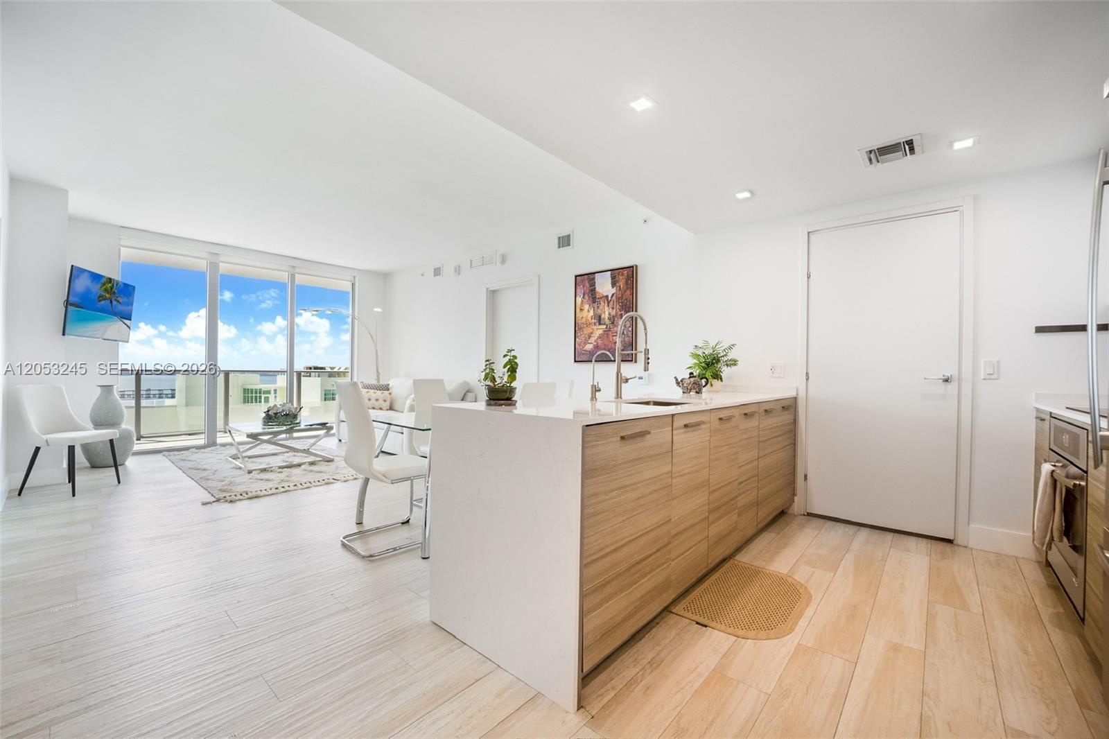 A modern kitchen with wood-toned cabinets and a white island opens into a living area — 1300 Brickell Bay Dr # 3004, Miami FL 33131, MIAMI, FL