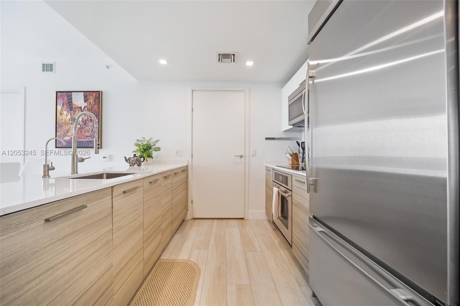 A modern kitchen features light wood cabinetry, stainless steel appliances, and white countertops — 1300 Brickell Bay Dr # 3004, Miami FL 33131, MIAMI, FL