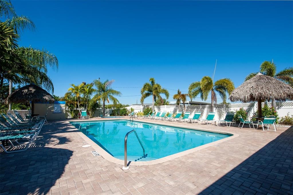 An outdoor swimming pool surrounded by lounge chairs, palm trees, and two tiki huts — 1000 COVE CAY DRIVE UNIT 5E, CLEARWATER, FL