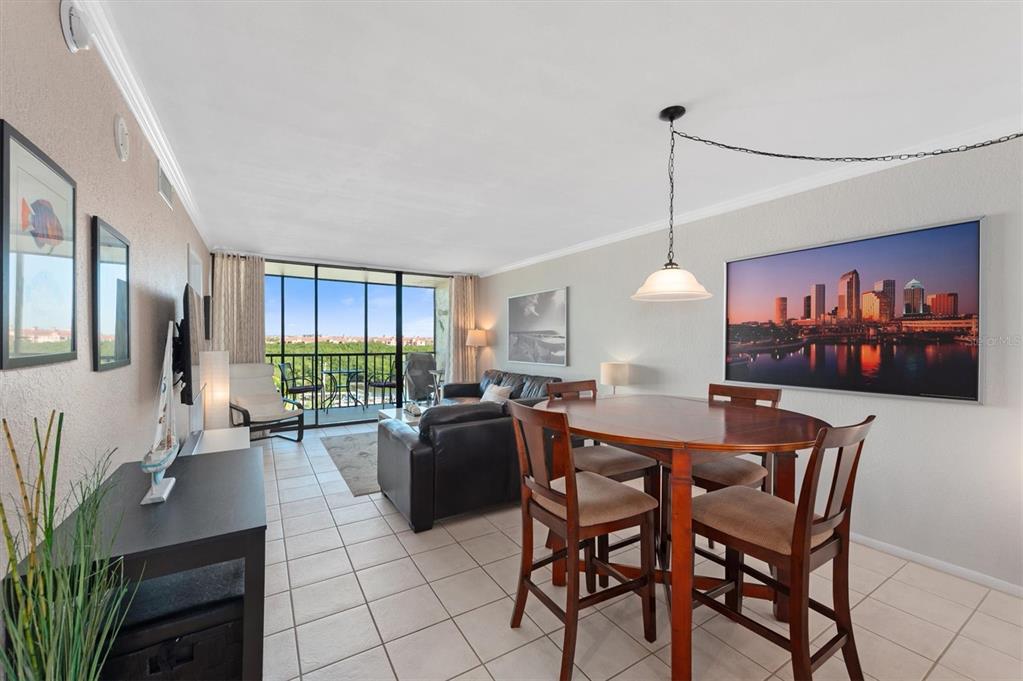 A combined living and dining area with tile floors, a balcony, and city skyline art — 1000 COVE CAY DRIVE UNIT 5E, CLEARWATER, FL