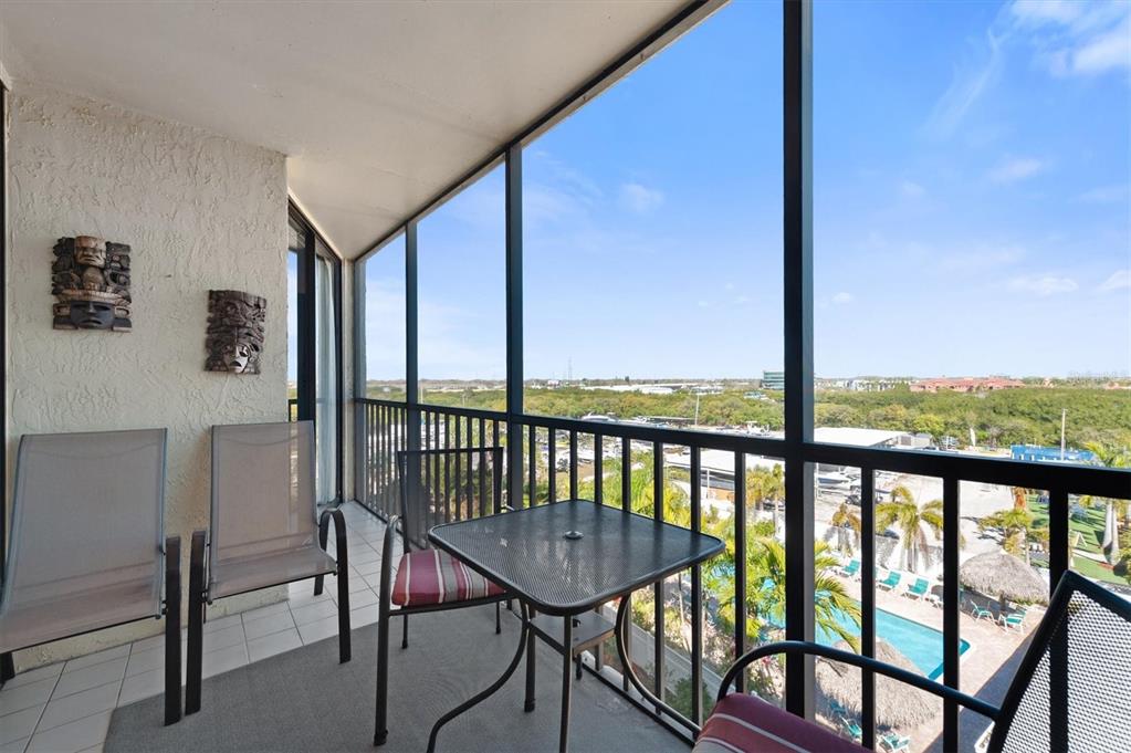 A screened-in balcony features patio furniture, wall-mounted masks, and a view of a swimming pool — 1000 COVE CAY DRIVE UNIT 5E, CLEARWATER, FL