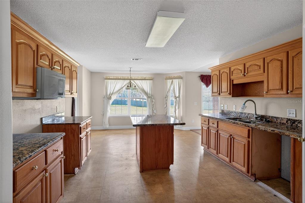 A kitchen with wood cabinets, granite countertops, a central island, and an adjacent dining area — 953 CHESAPEAKE TRAIL, CANTONMENT, FL