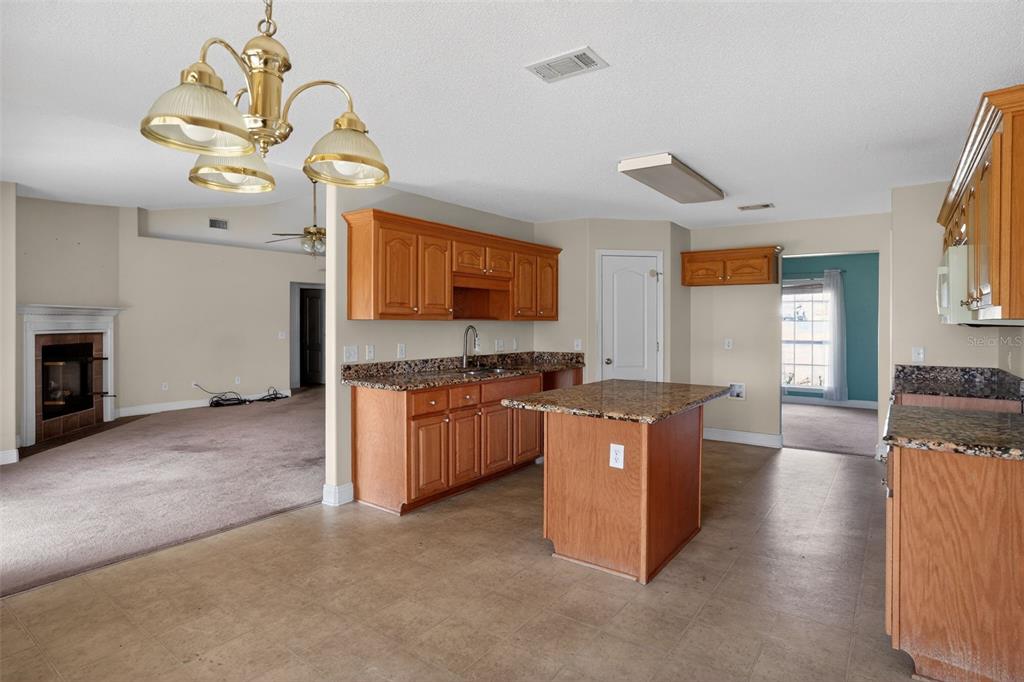 A kitchen with wood cabinets, granite countertops, and a center island opens to a living area — 953 CHESAPEAKE TRAIL, CANTONMENT, FL