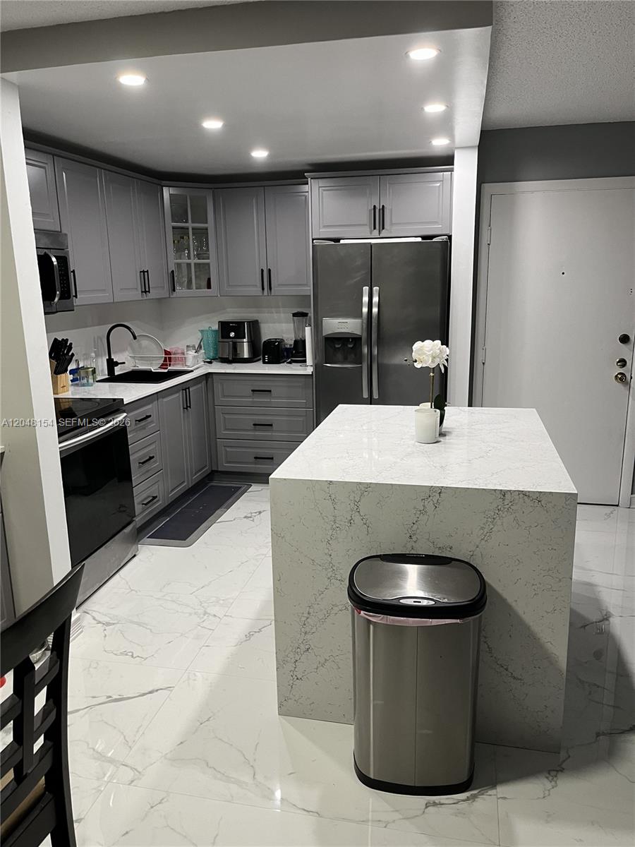 A kitchen features grey cabinets, stainless steel appliances, and a white quartz-topped island — 819 NE 199th St # 101, Miami FL 33179, MIAMI, FL