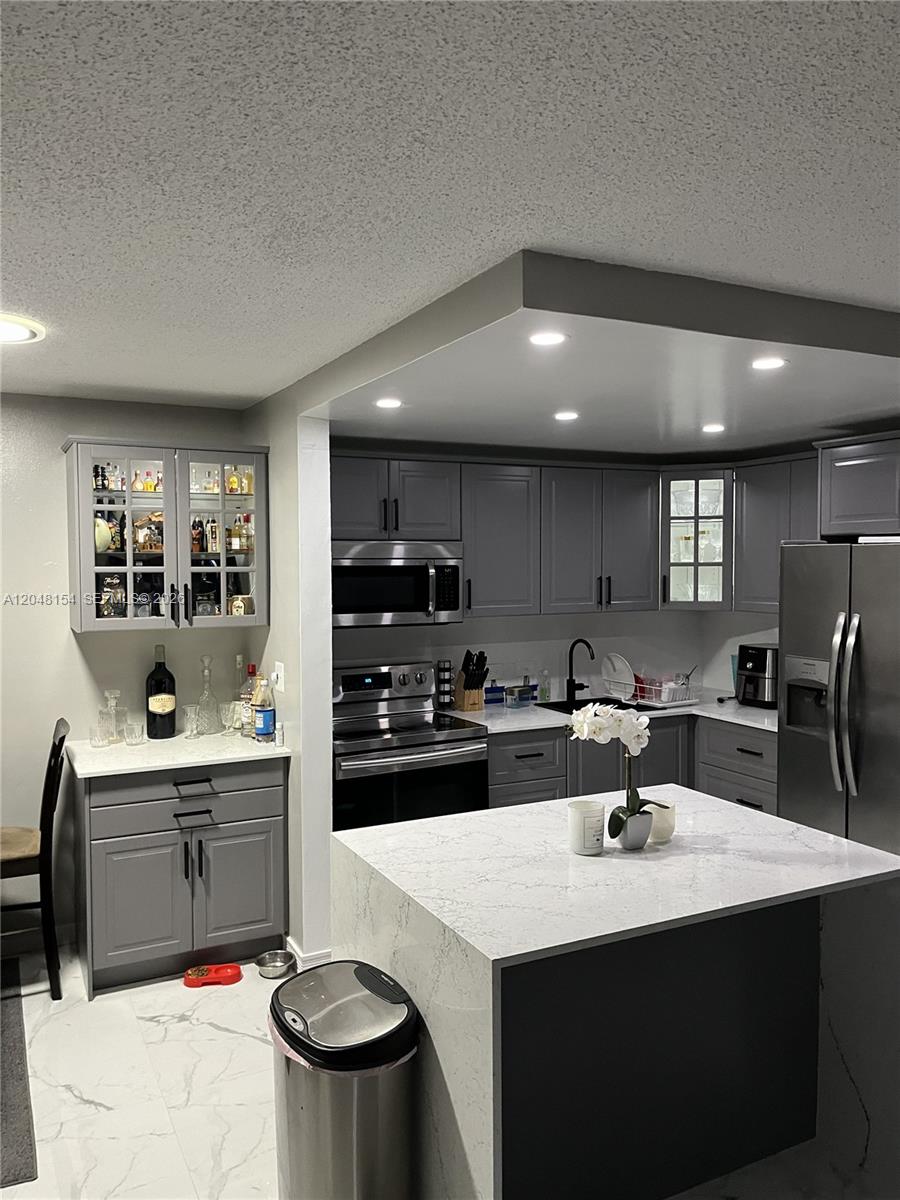 A modern kitchen features gray cabinetry, a white quartz island, and a separate bar area — 819 NE 199th St # 101, Miami FL 33179, MIAMI, FL