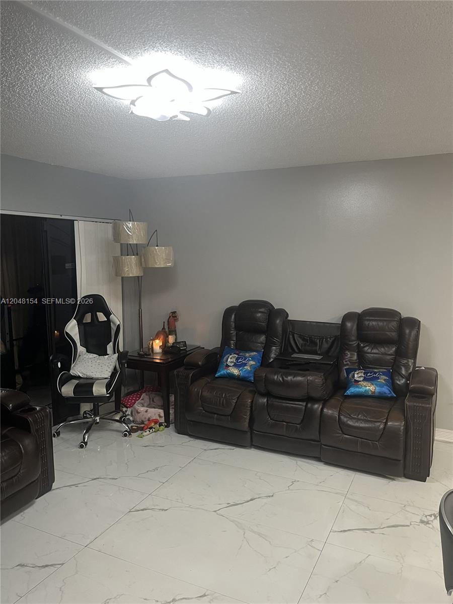A living room features white marble-look tile flooring, a brown leather sofa, and a gaming chair — 819 NE 199th St # 101, Miami FL 33179, MIAMI, FL