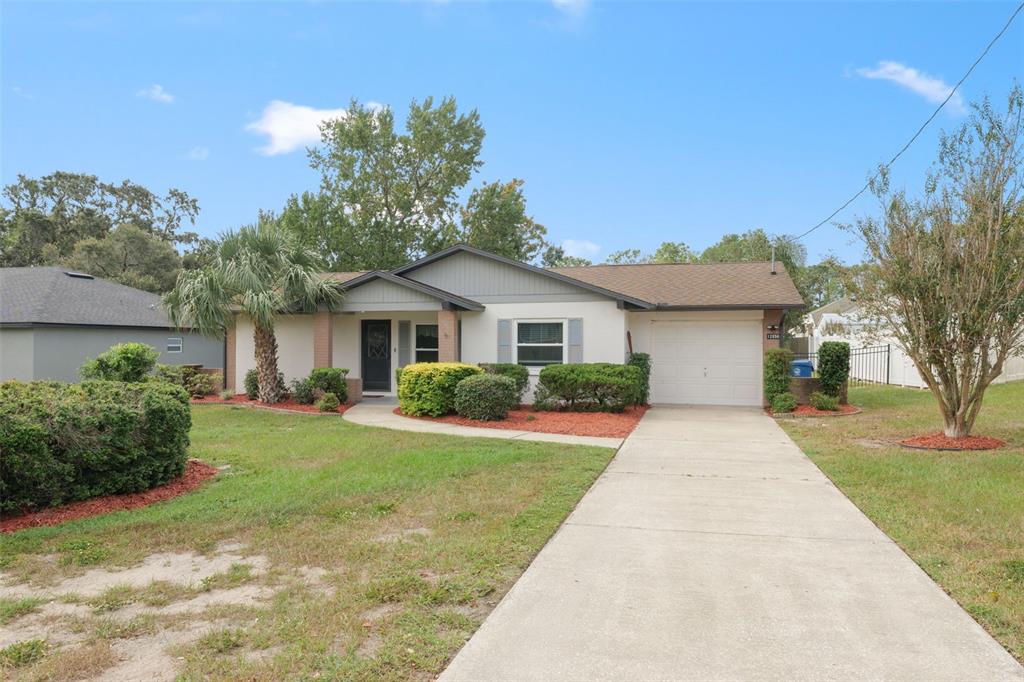 A single-story house with a white exterior, a front-facing garage, and a landscaped front yard — 12056 CRADOCK STREET, SPRING HILL, FL