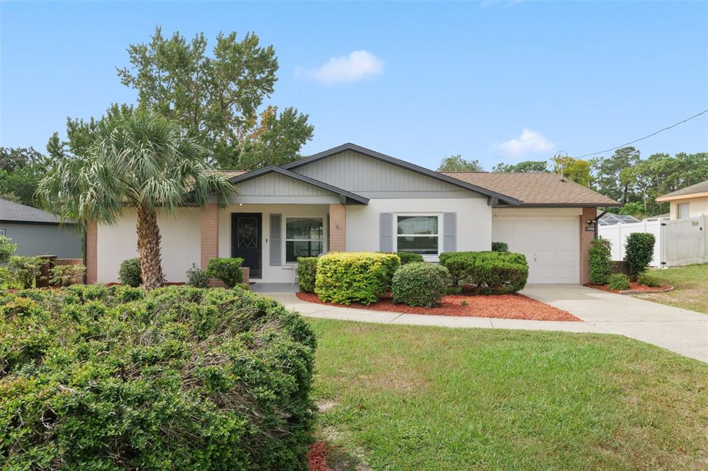 A single-story house with a white facade, brick accents, a palm tree, and a garage — 12056 CRADOCK STREET, SPRING HILL, FL