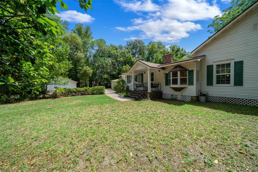 A white house with green shutters and a covered porch sits beside a grassy yard — 1985 NE 97TH STREED ROAD, ANTHONY, FL