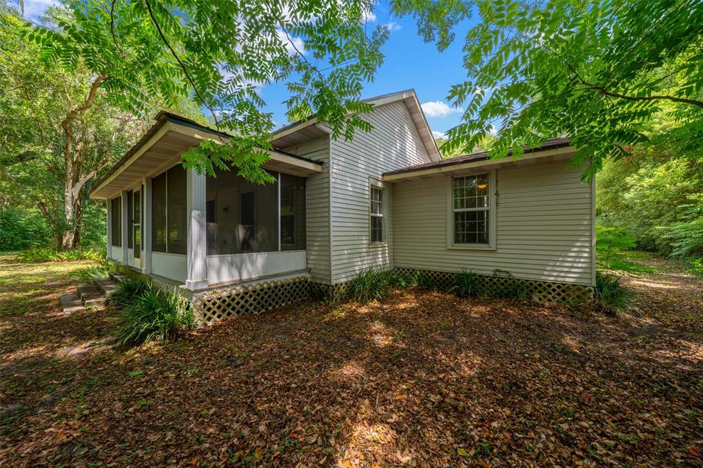 A beige house with a screened-in porch sits in a wooded area covered in leaves — 1985 NE 97TH STREED ROAD, ANTHONY, FL
