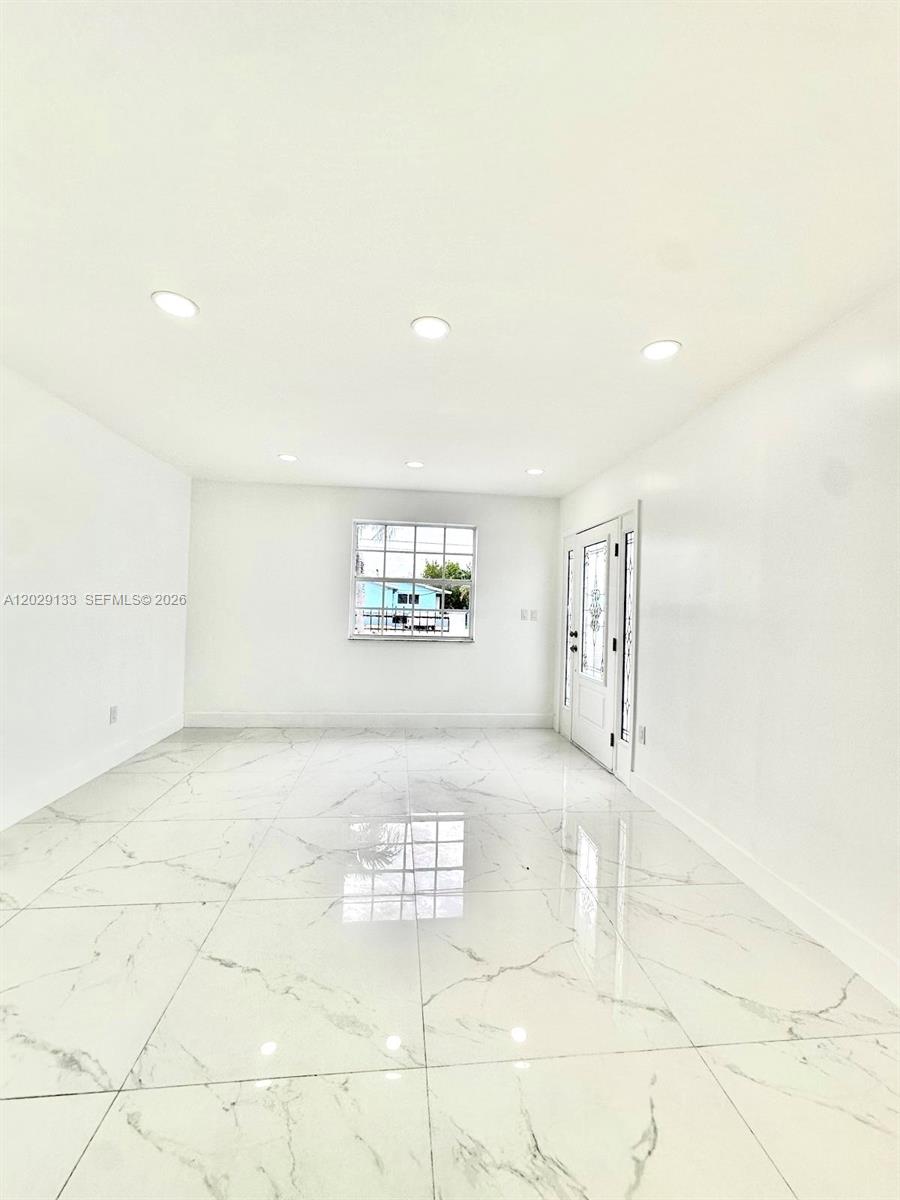 A bright, empty room features white walls, recessed lighting, and white marble-patterned tile flooring — HIALEAH, FL