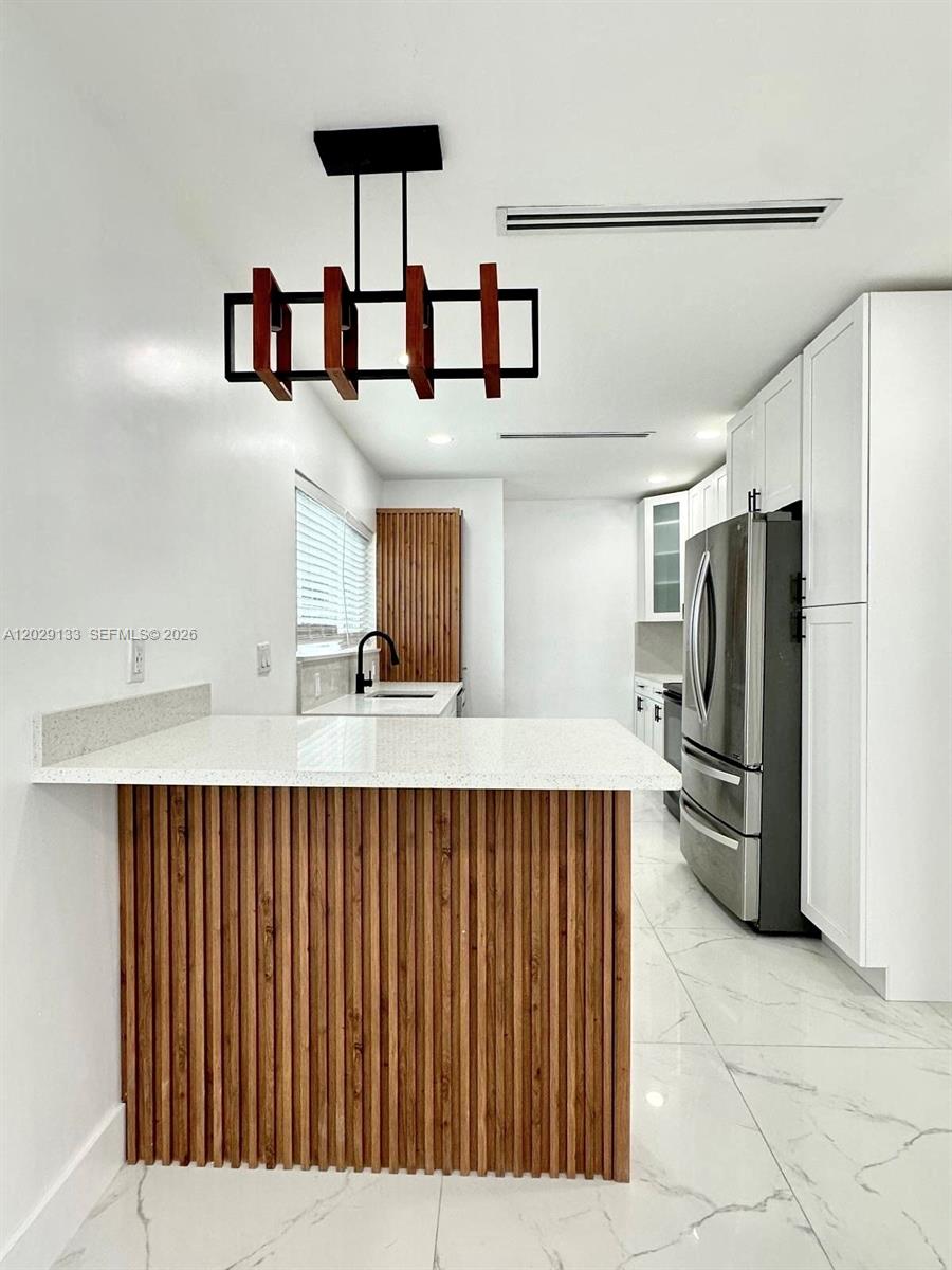 A modern kitchen features white cabinets, a slatted wood island, and a geometric pendant light — HIALEAH, FL