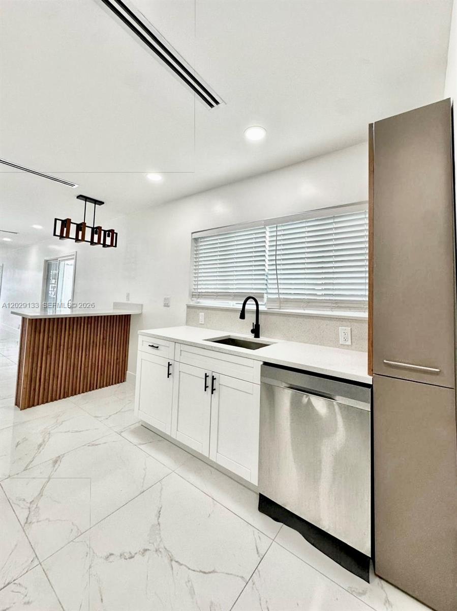 A modern kitchen features white cabinets, a stainless steel dishwasher, and a wood-slatted island — HIALEAH, FL