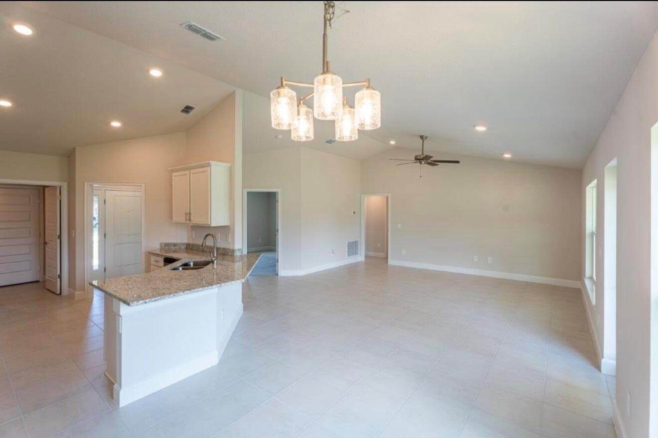 An open-concept living area features a kitchen with granite countertops and a dining room chandelier — 7903 Penny Lane, Fort Pierce FL 34951, FORT PIERCE, FL