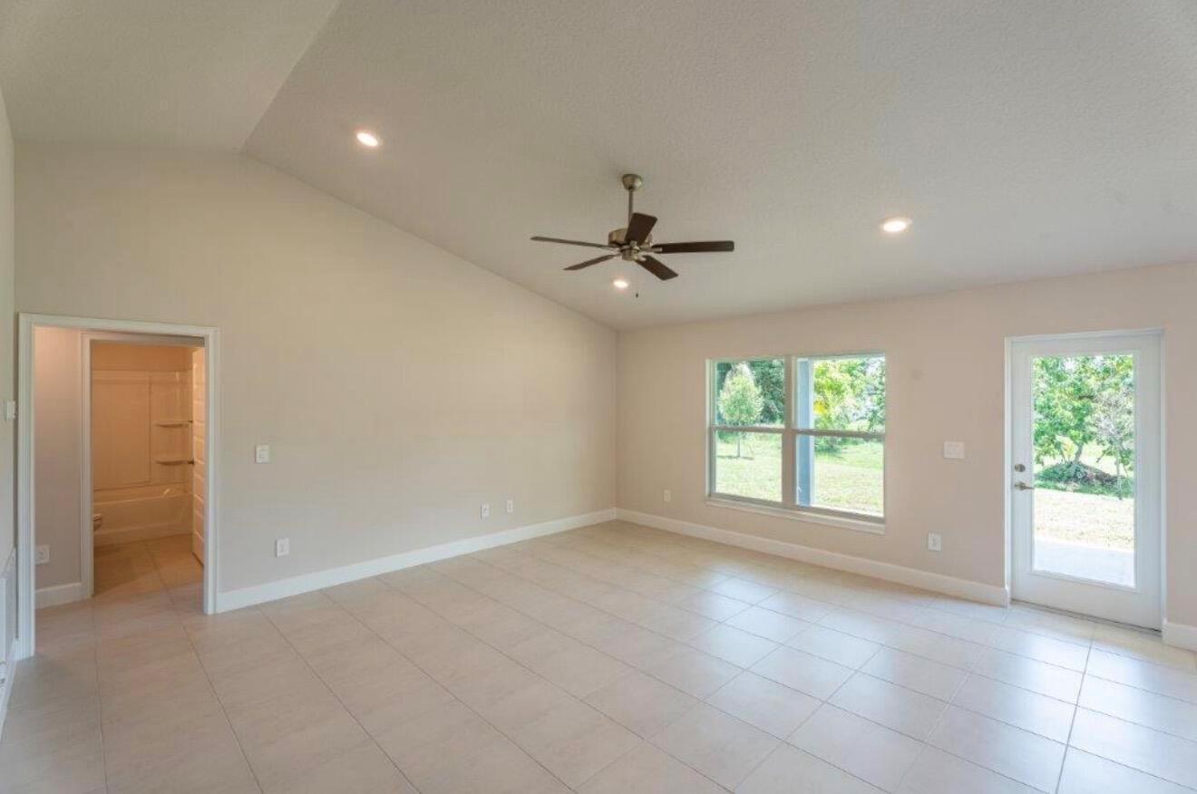 An empty living room features light-colored tile flooring, a vaulted ceiling, and a glass door — 7903 Penny Lane, Fort Pierce FL 34951, FORT PIERCE, FL