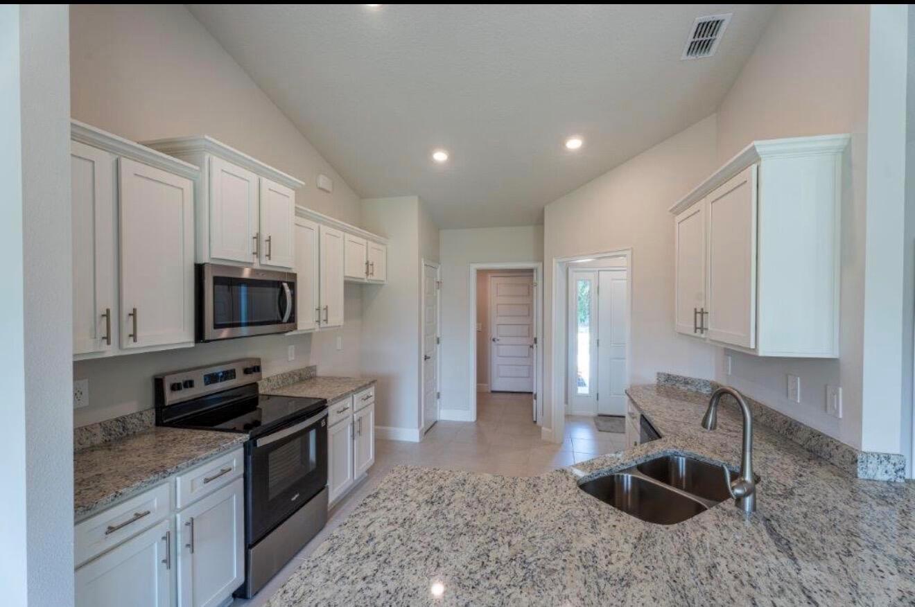 A kitchen with white cabinets, granite countertops, stainless steel appliances, and a double sink — 7903 Penny Lane, Fort Pierce FL 34951, FORT PIERCE, FL