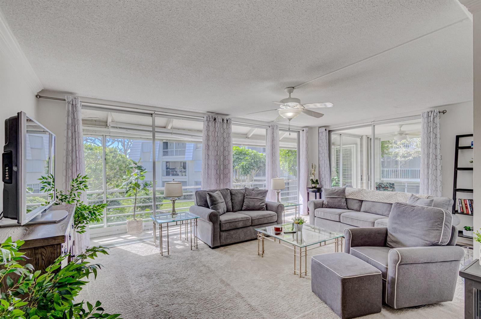 A living room features gray furniture, a glass coffee table, and large sliding glass doors — 1201 Sugar Sands Boulevard, West Palm Beach FL 33404, WEST PALM BEACH, FL