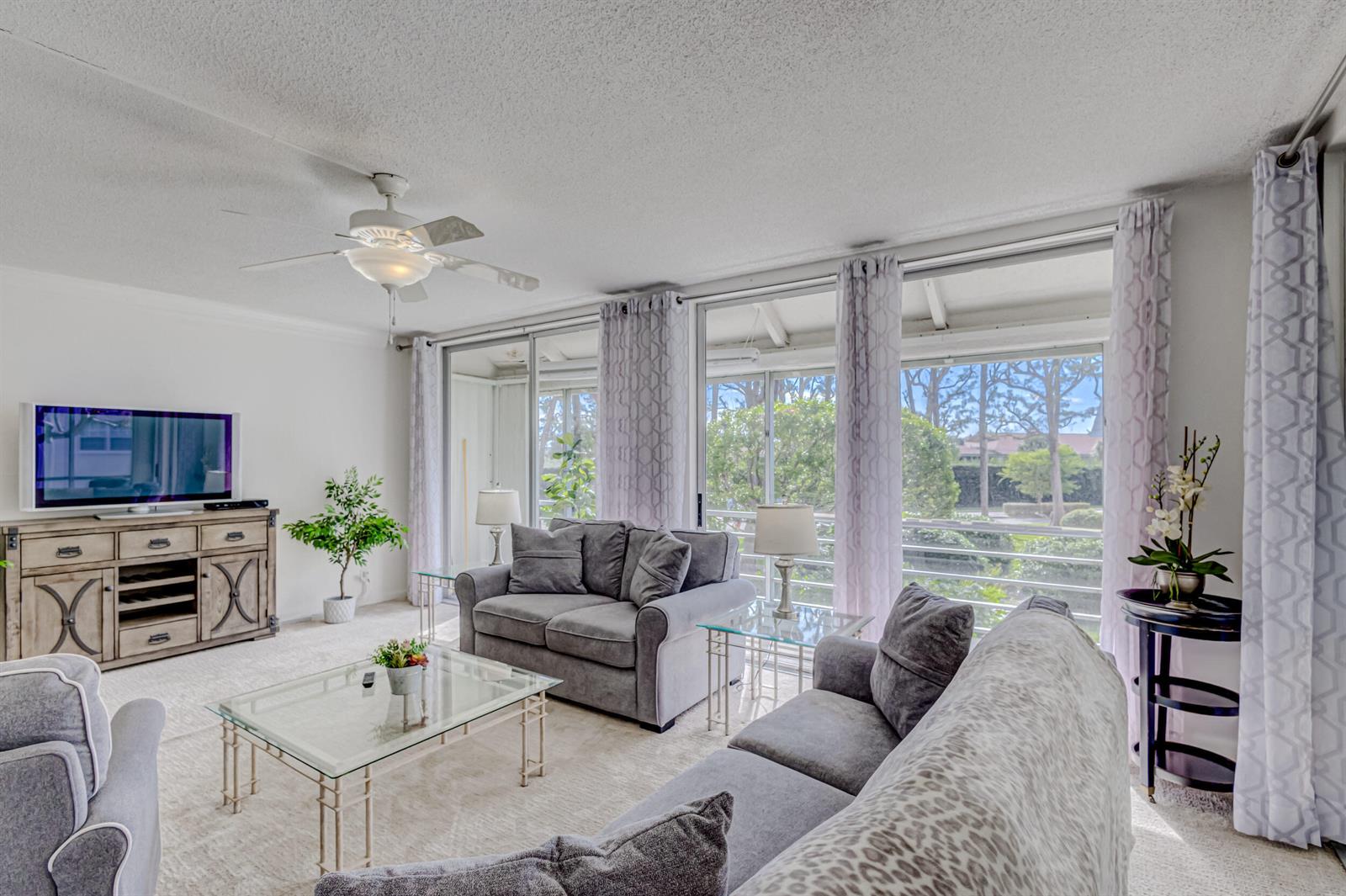 A living room features gray sofas, a glass coffee table, and large sliding glass doors — 1201 Sugar Sands Boulevard, West Palm Beach FL 33404, WEST PALM BEACH, FL
