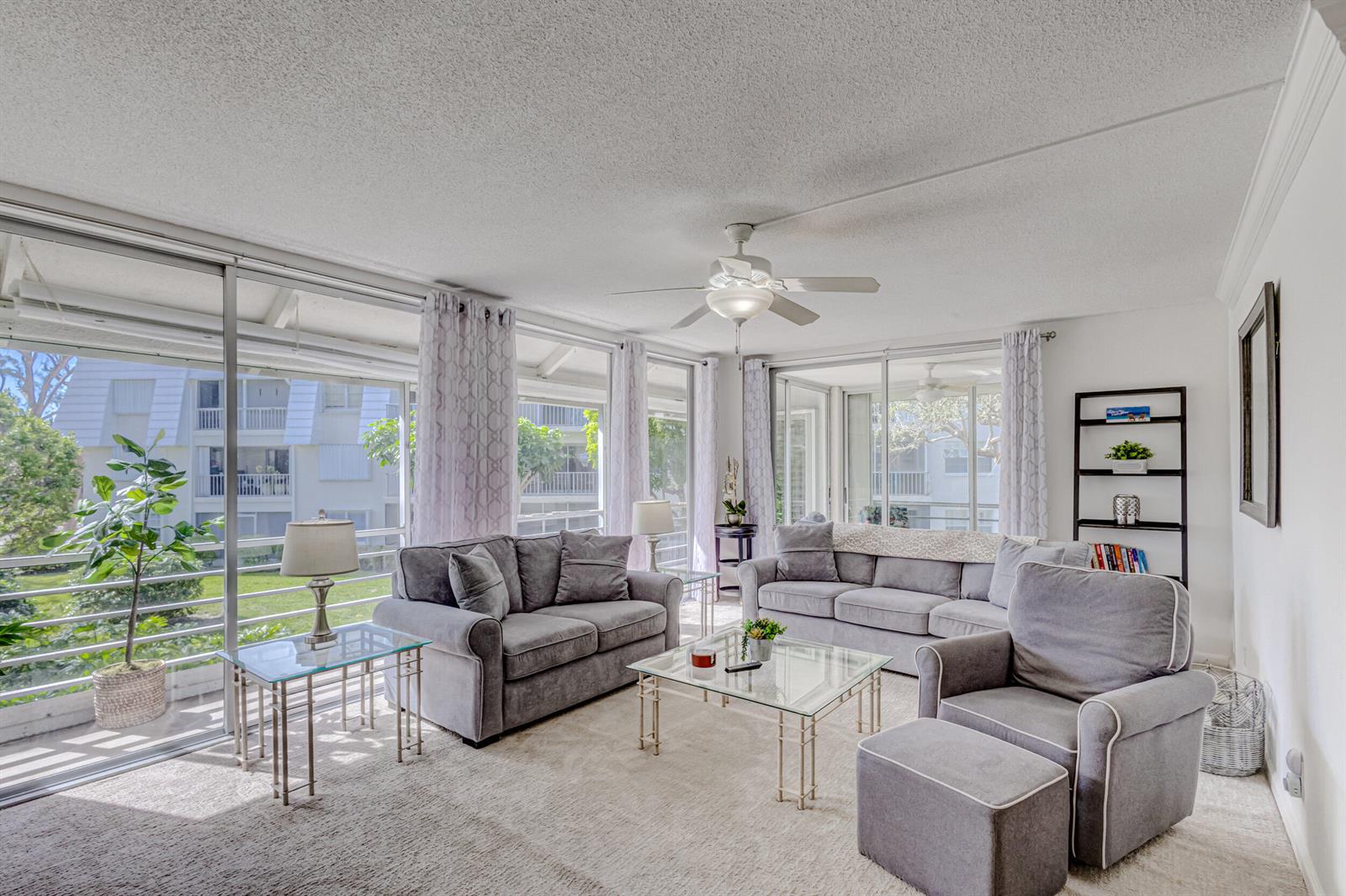 A bright living room features gray furniture, a glass coffee table, and large sliding doors — 1201 Sugar Sands Boulevard, West Palm Beach FL 33404, WEST PALM BEACH, FL