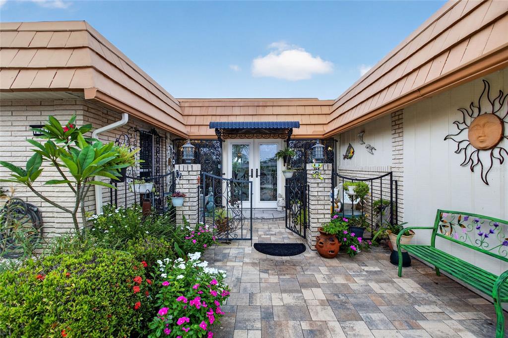 A paved courtyard leads to a glass-paned double door entrance with a metal awning — 1411 JACOBSON CIRCLE, SUN CITY CENTER, FL