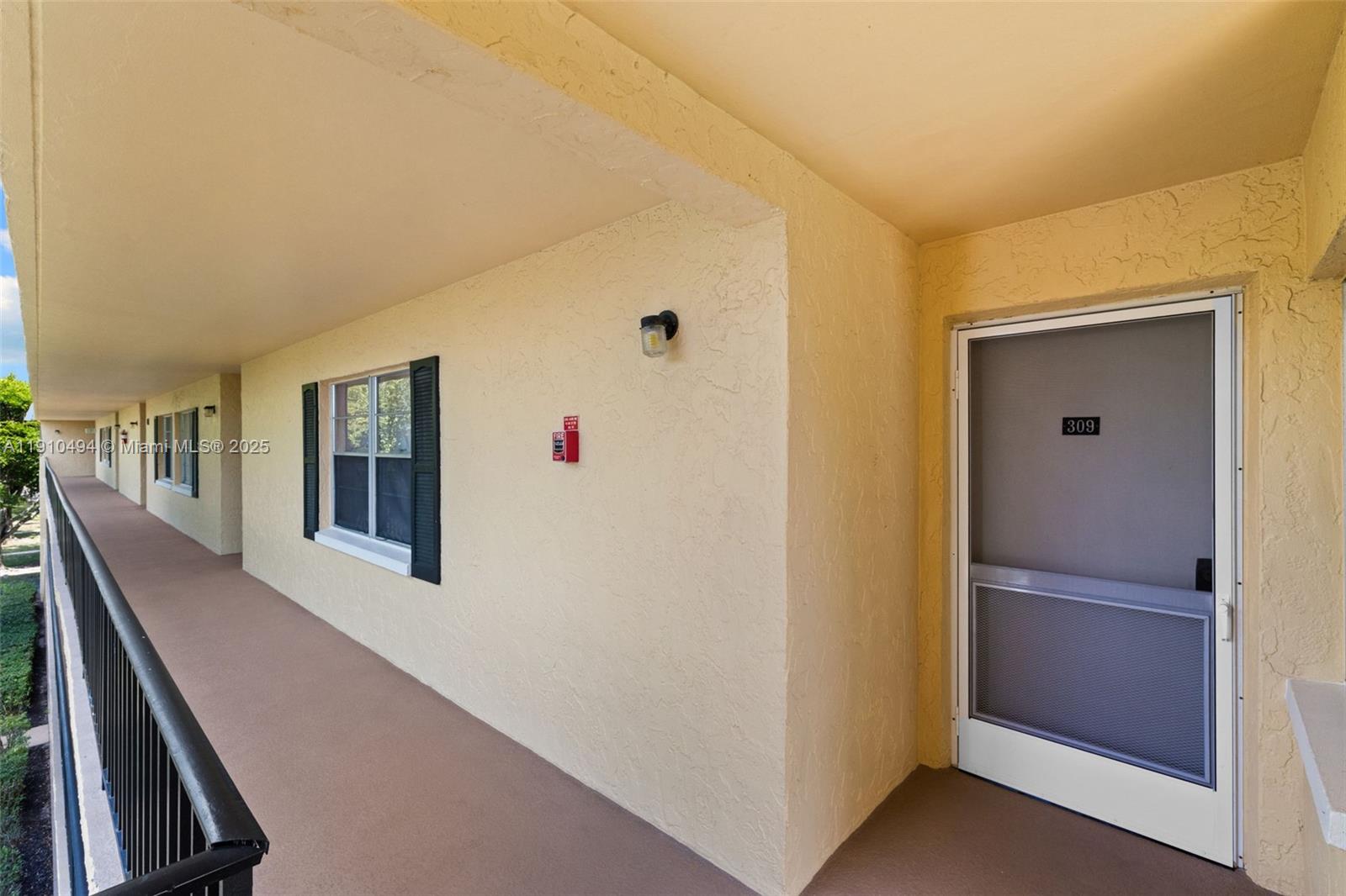 An exterior walkway features a beige stucco wall, a screen door numbered 309, and windows — 1087 Forest Lakes Drive # 309, Naples FL 34105, NAPLES, FL