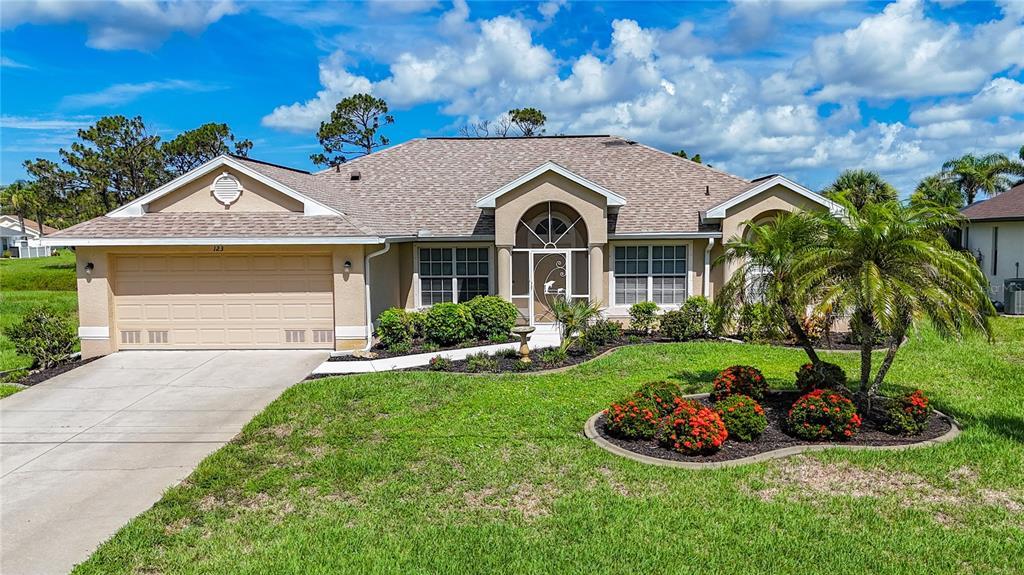 A tan, single-story suburban house features a two-car garage and a landscaped front yard — 123 MARKER ROAD, ROTONDA WEST, FL