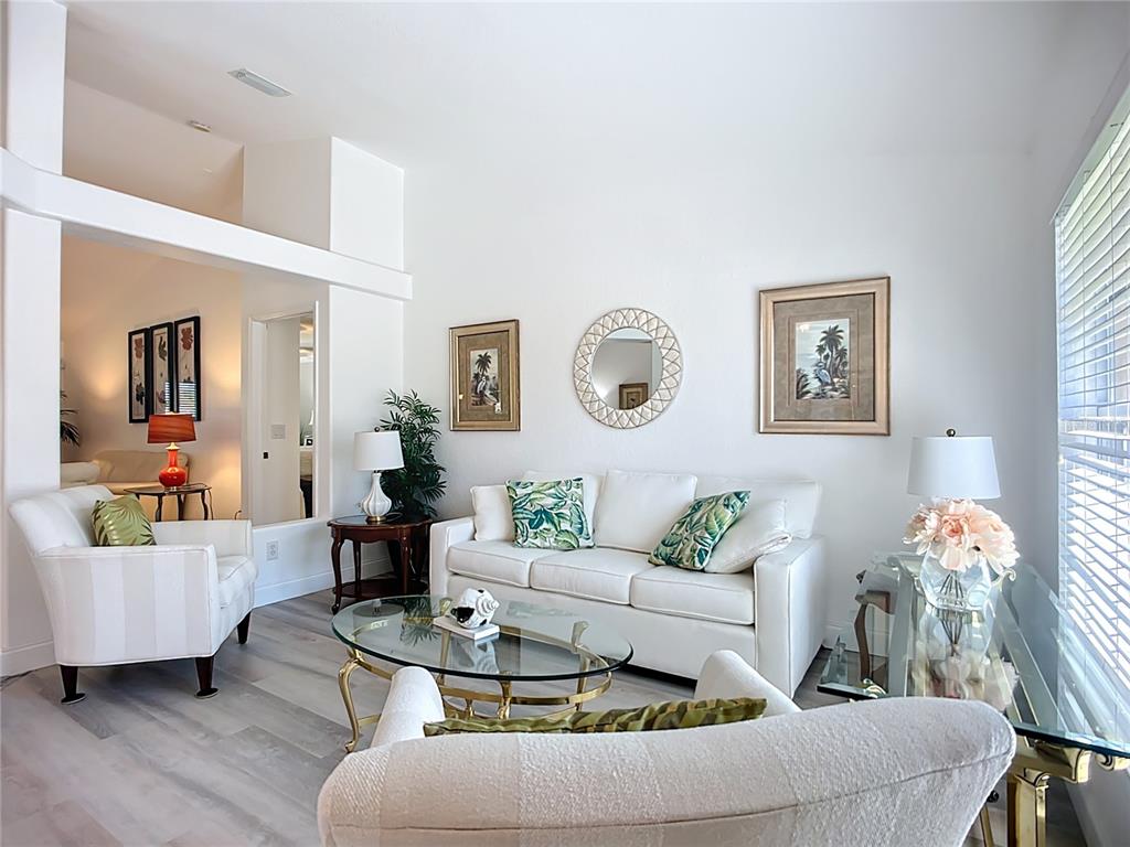 A bright living room features white furniture, a glass coffee table, and tropical-themed wall art — 123 MARKER ROAD, ROTONDA WEST, FL