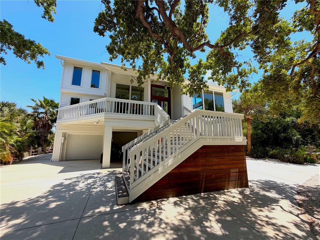 A white two-story house features a raised deck, wooden staircase, and a concrete driveway — 7025 MANASOTA KEY ROAD, ENGLEWOOD, FL