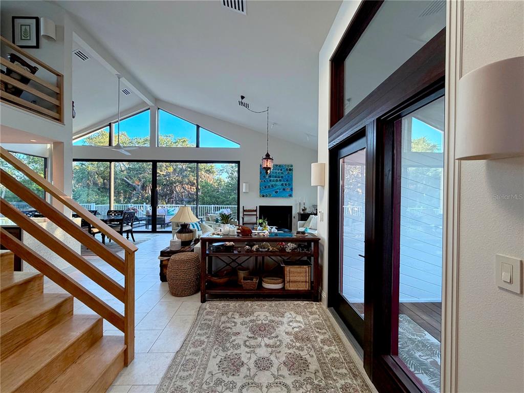 A bright living area features vaulted ceilings, large windows, a wooden staircase, and tile flooring — 7025 MANASOTA KEY ROAD, ENGLEWOOD, FL