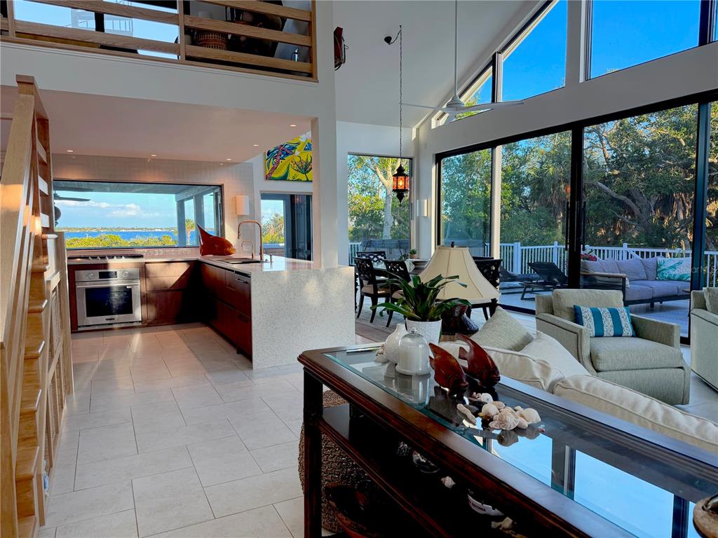 An open-concept living and kitchen area features large windows, tile flooring, and a wooden staircase — 7025 MANASOTA KEY ROAD, ENGLEWOOD, FL