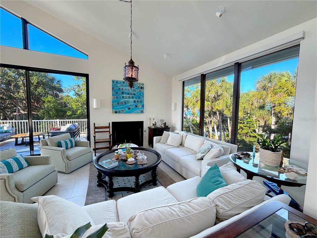 A bright living room features a vaulted ceiling, large windows, and a central fireplace — 7025 MANASOTA KEY ROAD, ENGLEWOOD, FL