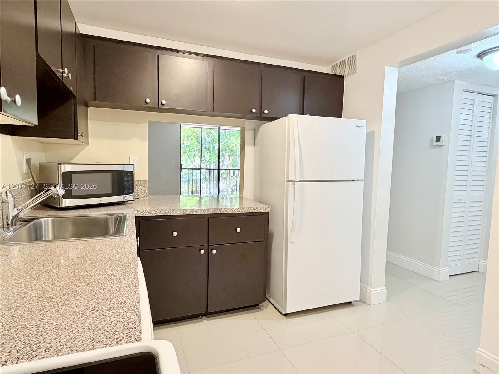 A kitchen features dark brown cabinets, speckled countertops, a white refrigerator, and a stainless sink — 450 Commodore Dr # 214, Plantation FL 33325, PLANTATION, FL
