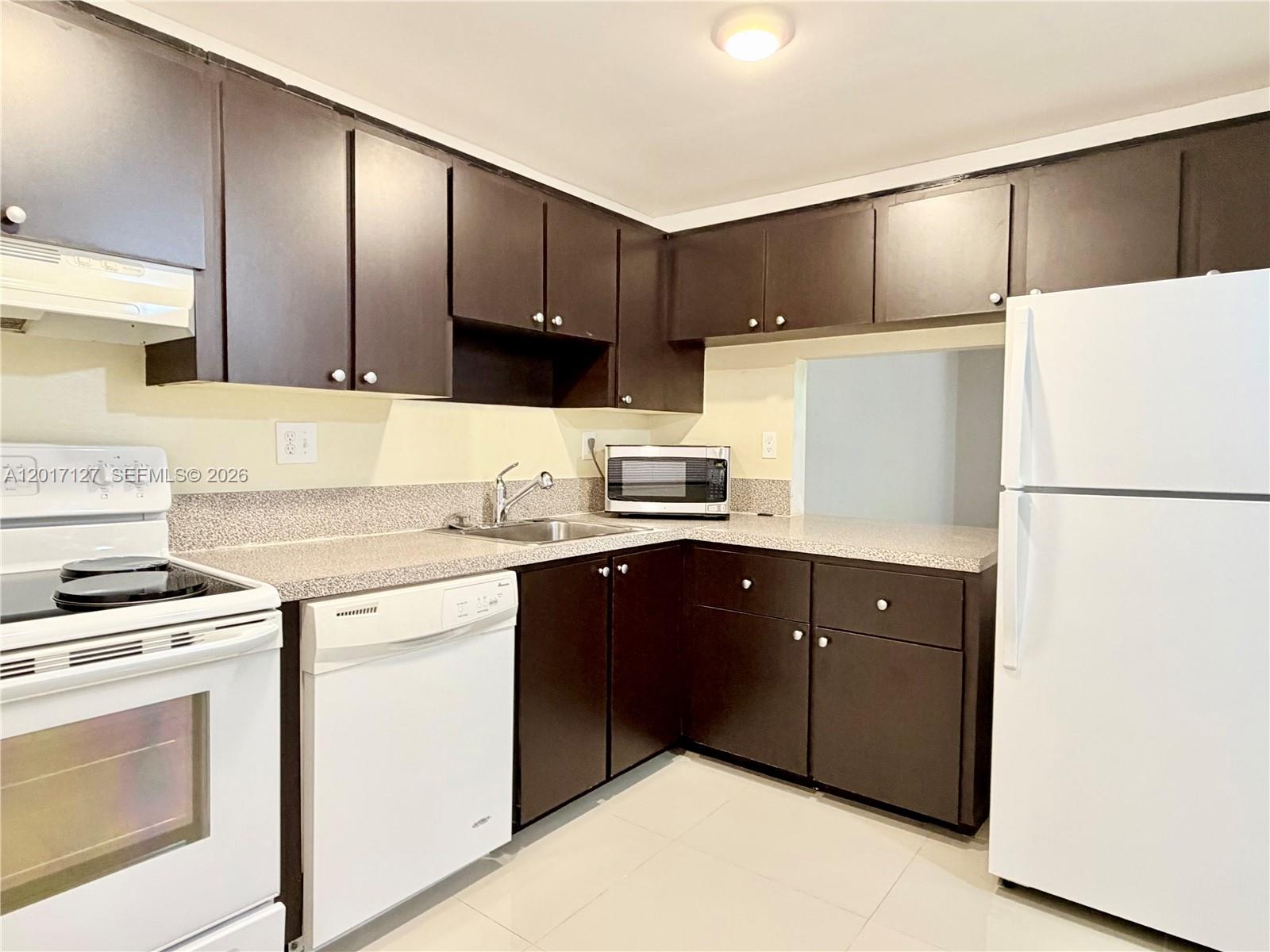 A kitchen features dark brown cabinets, white appliances, and speckled countertops — 450 Commodore Dr # 214, Plantation FL 33325, PLANTATION, FL