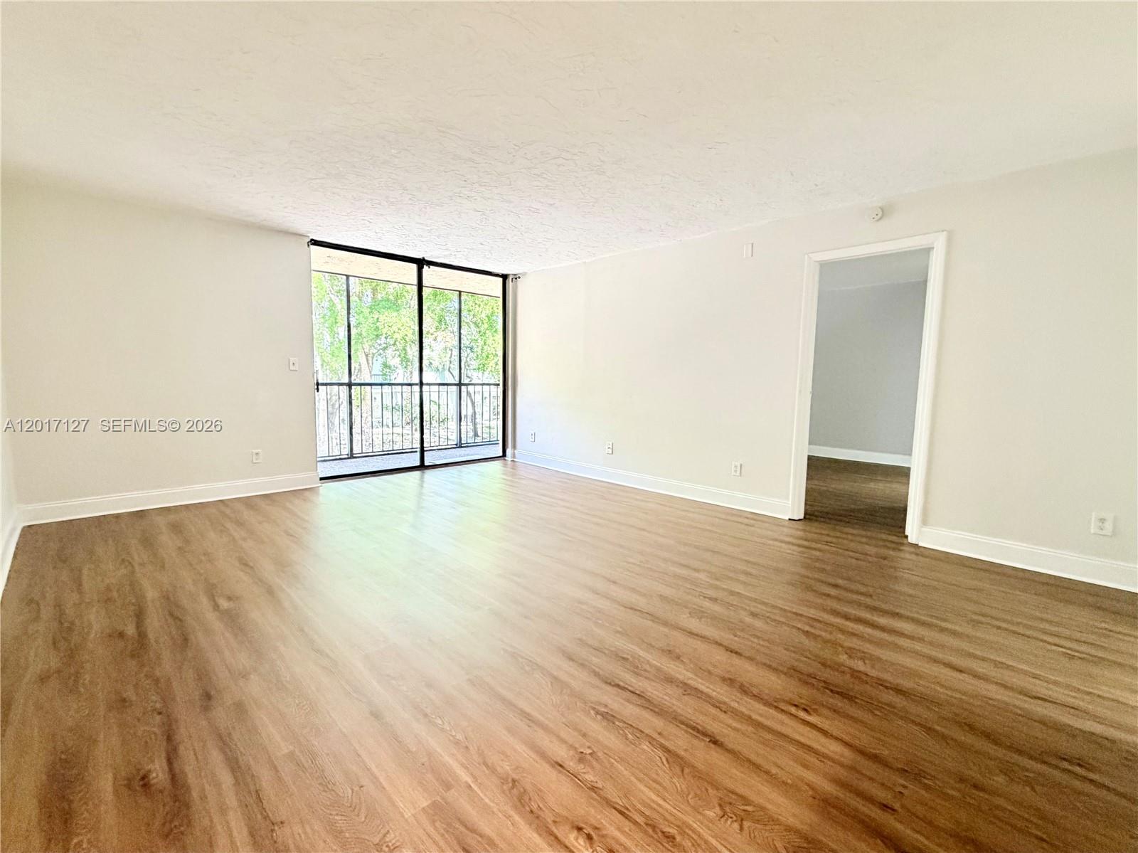 An empty room features light wood-look flooring, white walls, and a sliding glass door to a balcony — 450 Commodore Dr # 214, Plantation FL 33325, PLANTATION, FL
