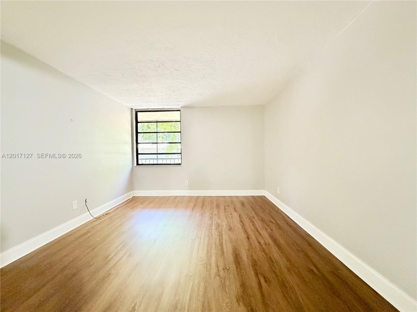 An empty room features light gray walls, wood-look flooring, and a window with security bars — 450 Commodore Dr # 214, Plantation FL 33325, PLANTATION, FL