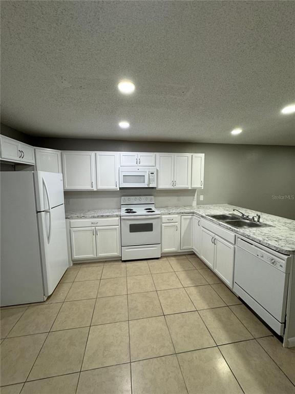 A kitchen features white cabinets, white appliances, a double sink, and light-colored tile flooring — 2526 ELM AVE, LAKE WALES, FL