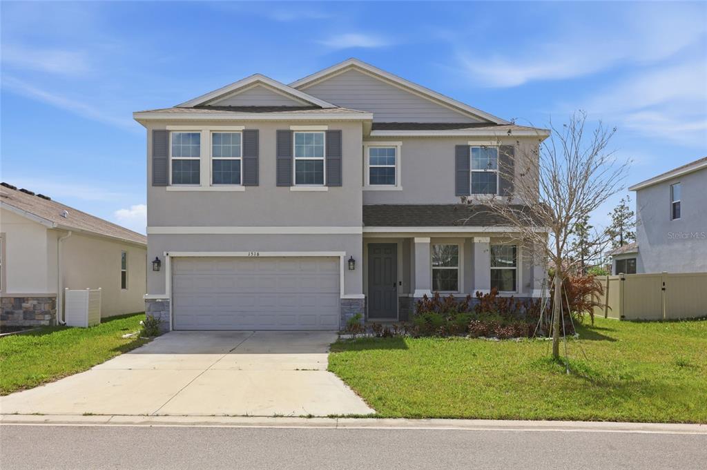 A two-story suburban house features a gray stucco exterior, a two-car garage, and a lawn — 1516 TROPICAL OASIS AVENUE, PLANT CITY, FL