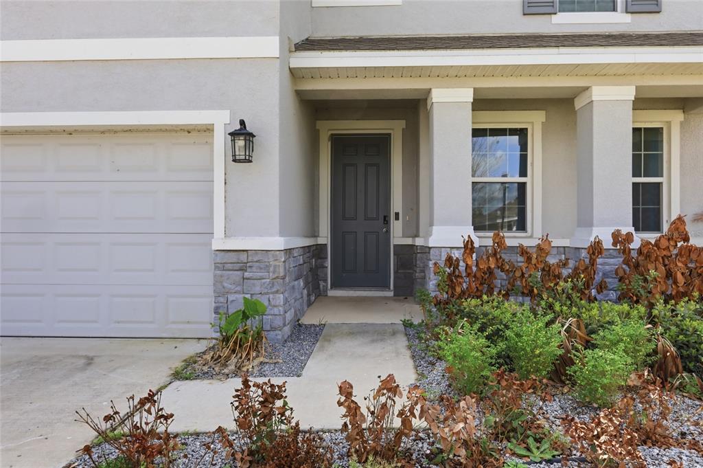 The exterior of a house features a gray front door, stone siding, and a garage — 1516 TROPICAL OASIS AVENUE, PLANT CITY, FL
