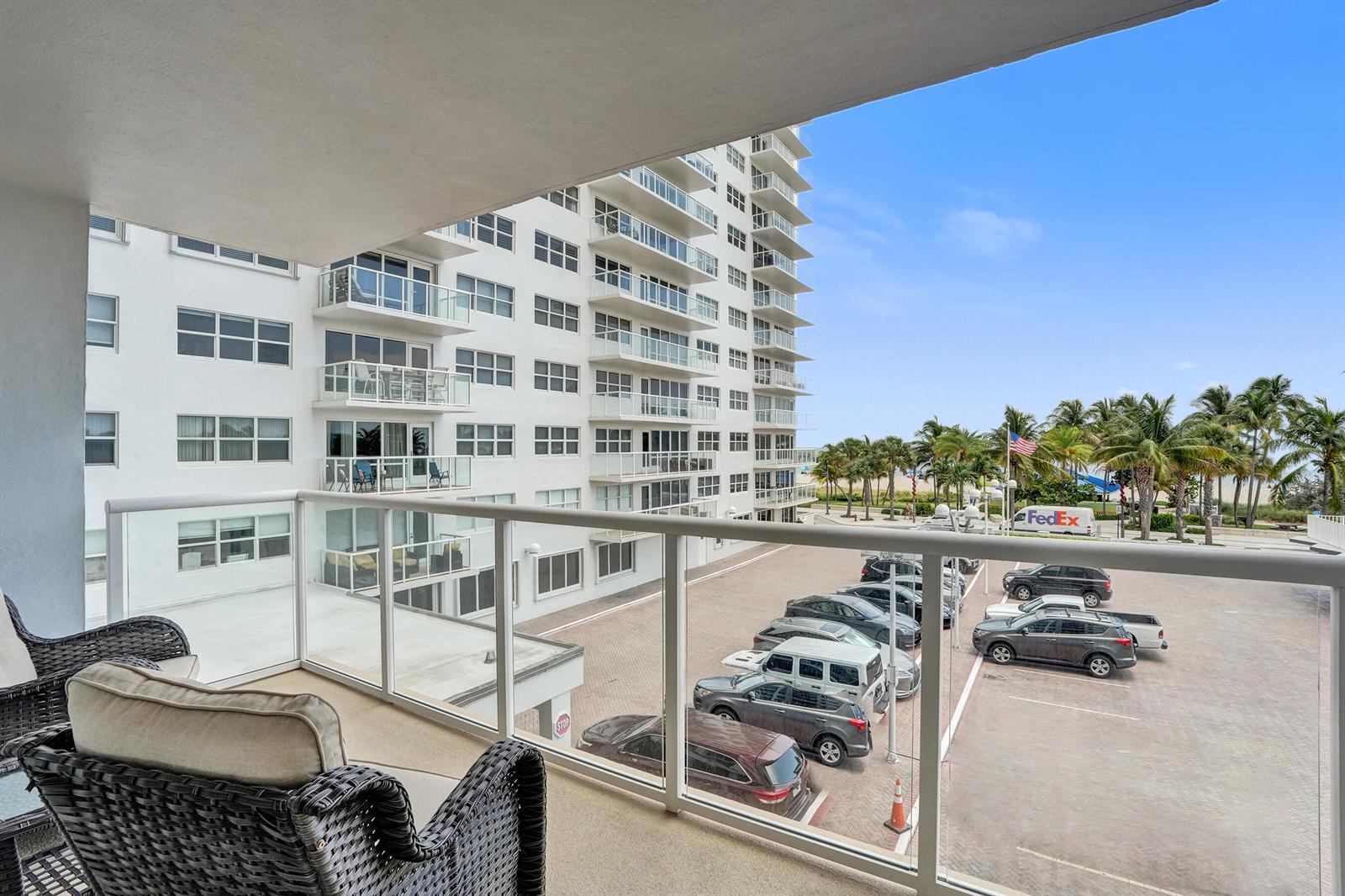 A balcony with wicker chairs overlooks a parking lot and a tall residential building — 111 N Pompano Beach Boulevard # 411, Pompano Beach FL 33062, POMPANO BEACH, FL