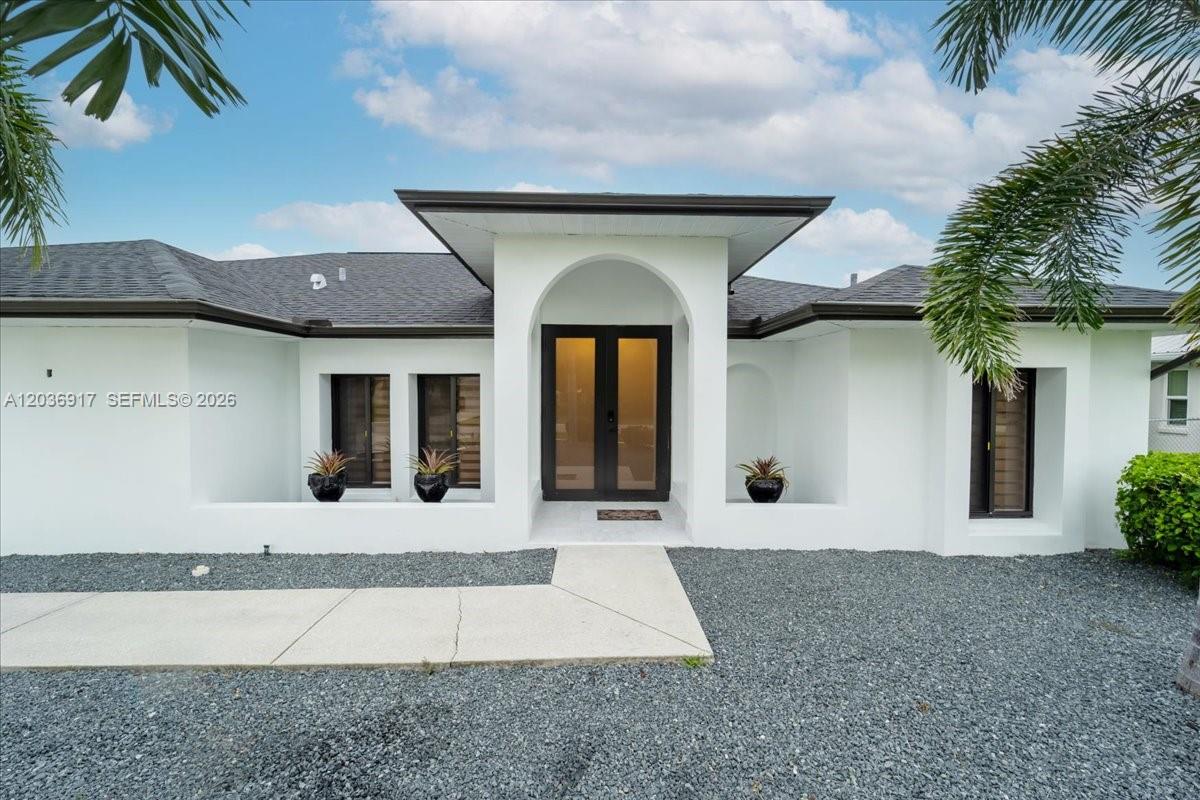 A white single-story house features a central arched entryway with black double doors — 3728 SE 18 Ave, Cape Coral FL 33904, CAPE CORAL, FL