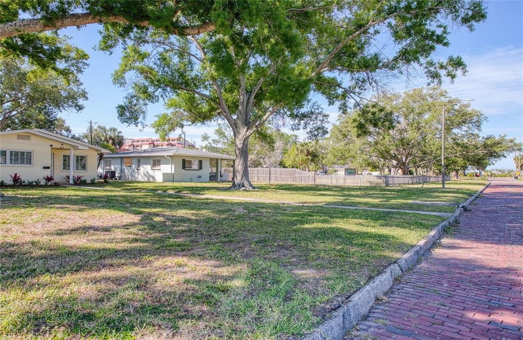 A grassy lot with large trees sits beside a one-story house and a brick street — 662 VILLAGRANDE AVENUE S, ST PETERSBURG, FL