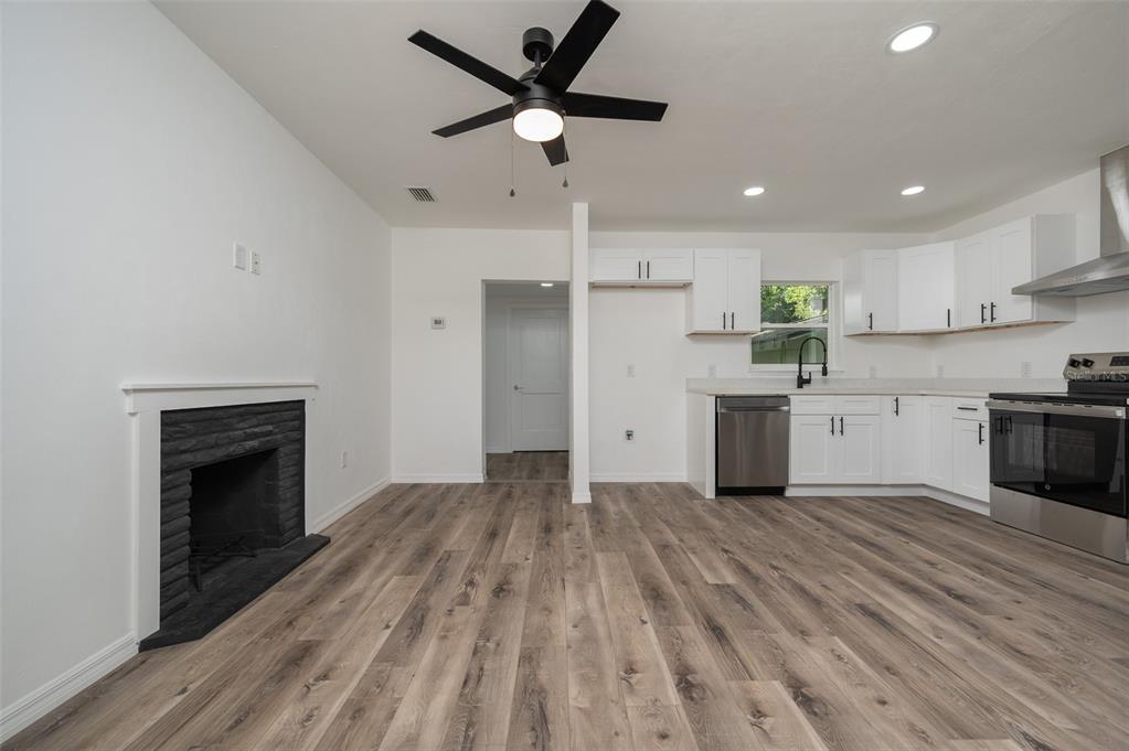 A kitchen and living area with white cabinets, stainless steel appliances, and a brick fireplace — 1935 NW 33RD AVENUE, GAINESVILLE, FL