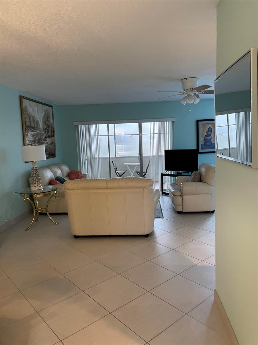 A living room features light blue walls, white leather furniture, tile flooring, and a balcony — 705 Lori Drive # 210, Palm Springs FL 33461, PALM SPRINGS, FL