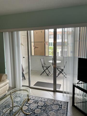 A living room looks out through sliding glass doors onto a tiled balcony with patio furniture — 705 Lori Drive # 210, Palm Springs FL 33461, PALM SPRINGS, FL