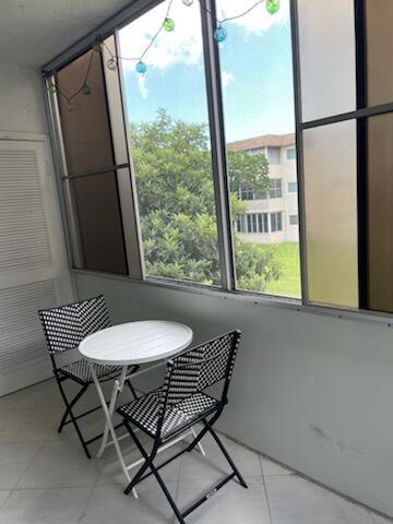 A small balcony features a white bistro table with two patterned chairs and large windows — 705 Lori Drive # 210, Palm Springs FL 33461, PALM SPRINGS, FL