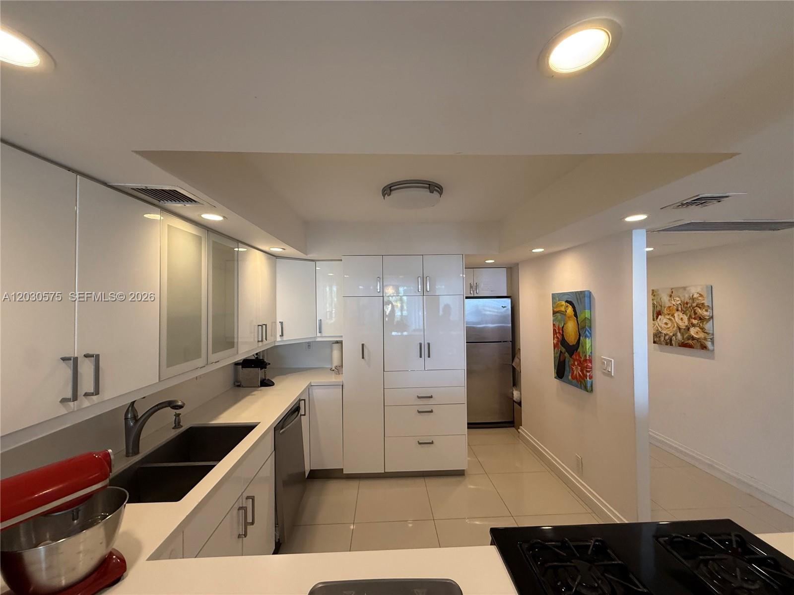 A modern kitchen features white glossy cabinets, stainless steel appliances, and light-colored tile flooring — 3140 S Ocean Dr # 310, Hallandale Beach FL 33009, HALLANDALE BEACH, FL