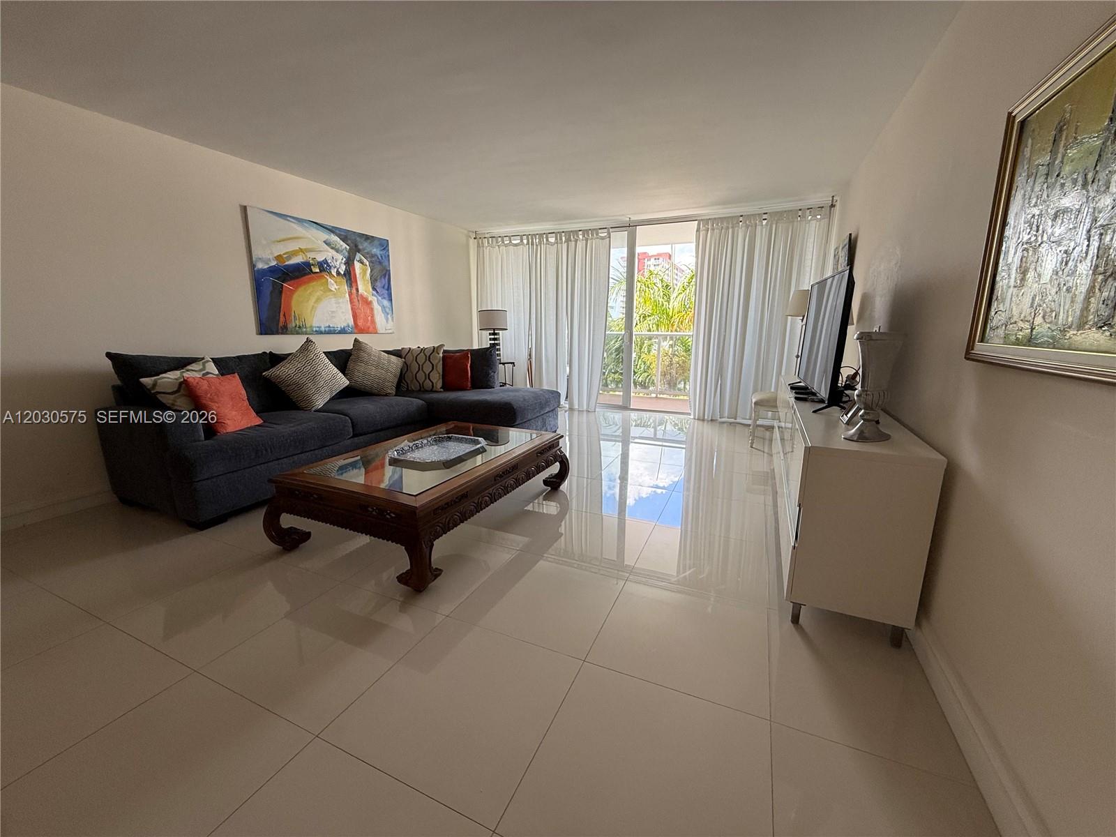 A living room features a dark sectional sofa, a wooden coffee table, and tile flooring — 3140 S Ocean Dr # 310, Hallandale Beach FL 33009, HALLANDALE BEACH, FL