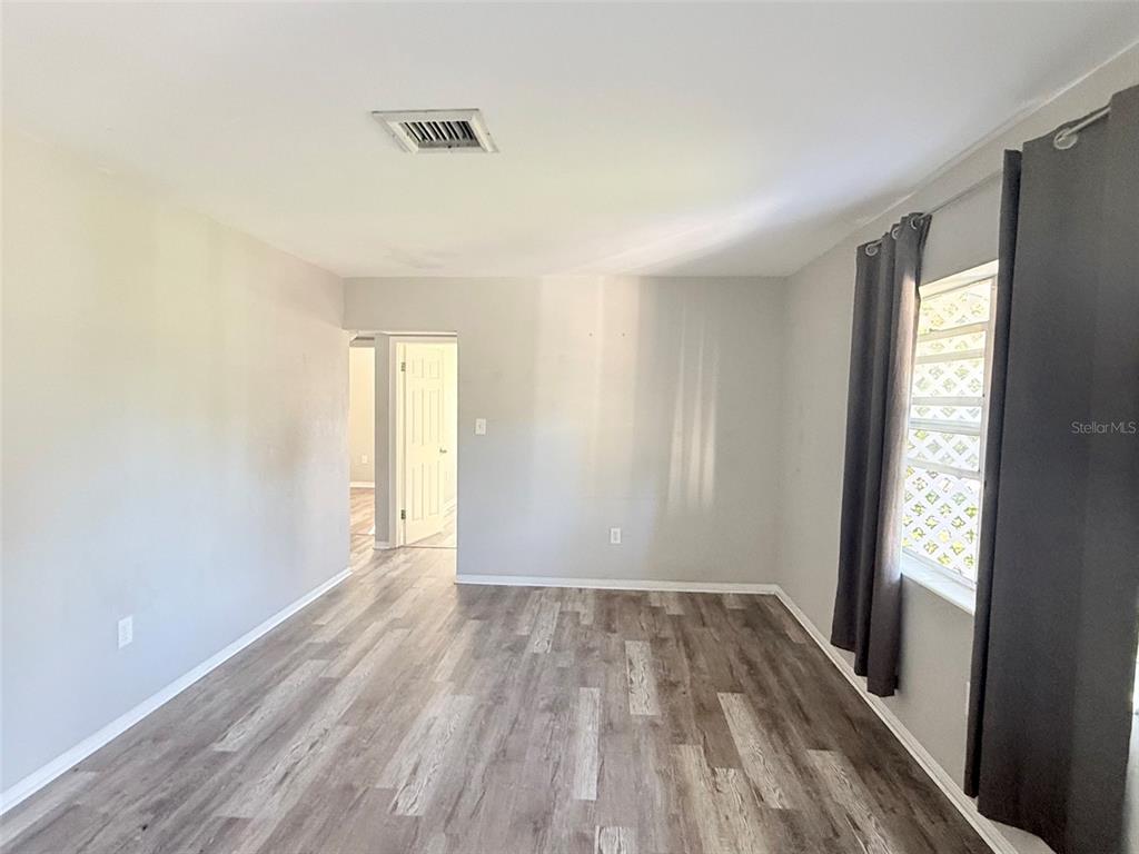 An empty room features light gray walls, wood-look flooring, and a window with dark curtains — 6041 43RD AVENUE N, ST PETERSBURG, FL